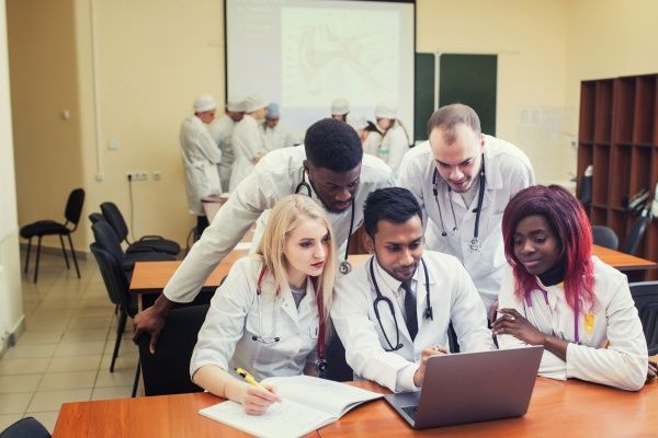A group of culturally diverse family nurse practitioner students studying together in front of a laptop in a nursing school classroom