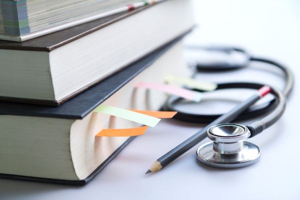 A stack of medical textbooks with a pencil and stethoscope beside them