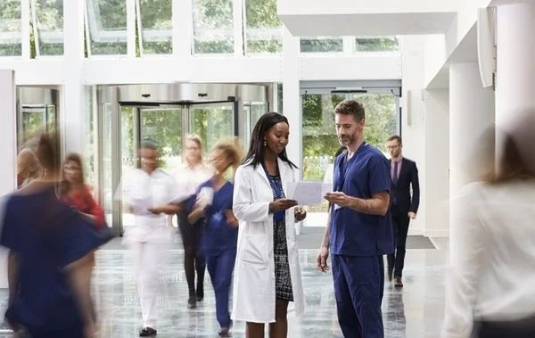 Female doctor and male nurse reviewing medical charts in the hospital while blurred out people walk by