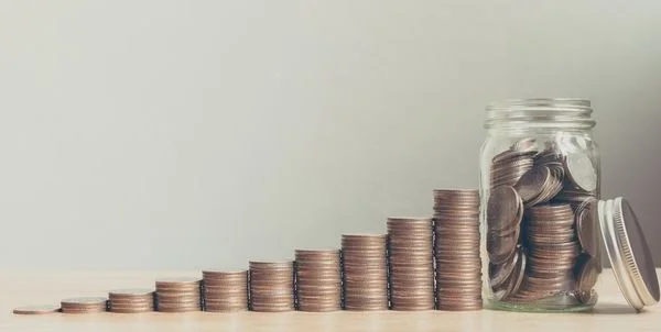 Stack of coins arranged in a staircase shape leading up to a jar of more coins