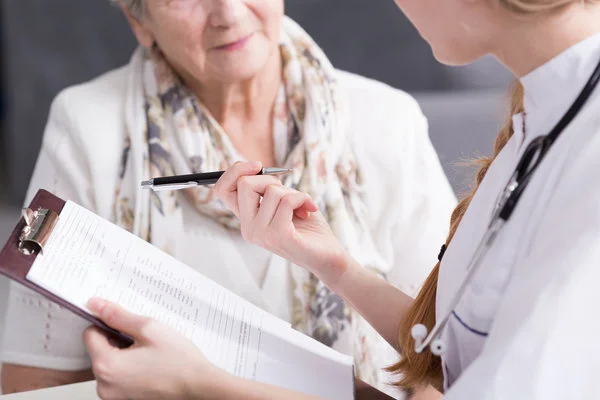 Nurse practitioner holding a clipboard and pen while talking to an elderly patient