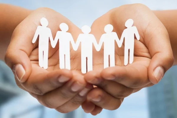 Close-up of a person's hands holding a white cardboard cutout of people holding hands