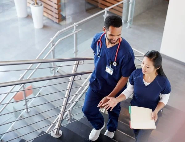 Male and female nurse walking up the stairs in a hospital while chatting