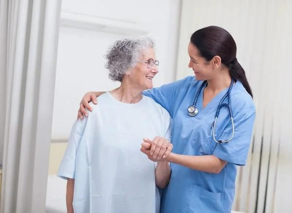 Female nurse in blue scrubs comforting a smiling elderly patient and resting her arm around her shoulders