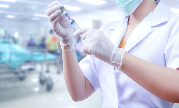 Close-up of medical practitioner wearing latex gloves and filling a syringe in a hospital setting