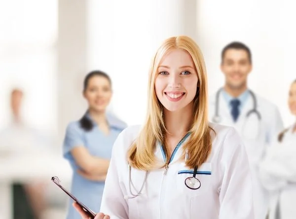 Smiling female nurse practitioner in a white lab coat with medical team behind her