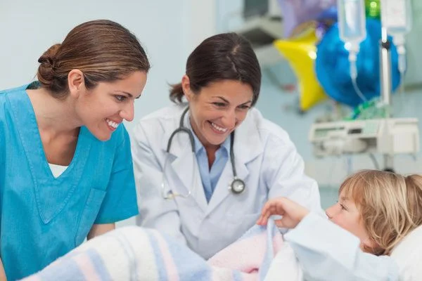 Female nurse and female doctor smiling and interacting with young boy in a hospital bed