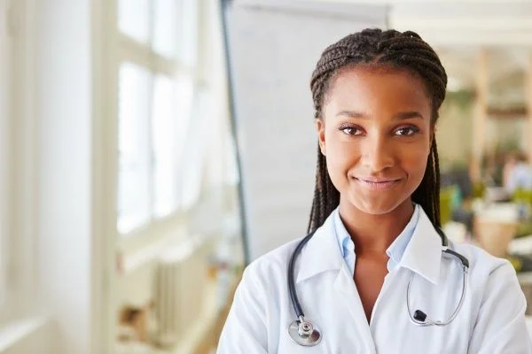 Smiling young African American female nurse practitioner looking confident and wearing a white lab coat with stethoscope