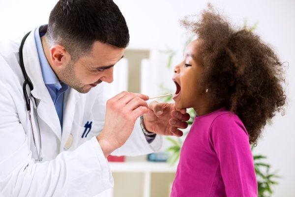 Male nurse practitioner performing a tonsil check on a young girl with frizzy hair