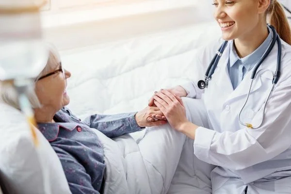 Smiling female nurse practitioner grasping the hand of an elderly female patient lying down in bed