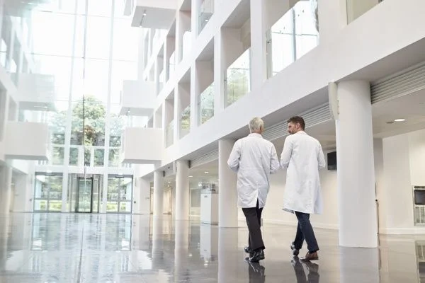 Two doctors in white lab coats walking down a modern-looking empty hospital atrium