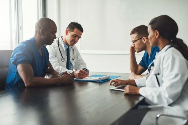 Two doctors and two nurses meeting in a hospital boardroom while one of them takes notes