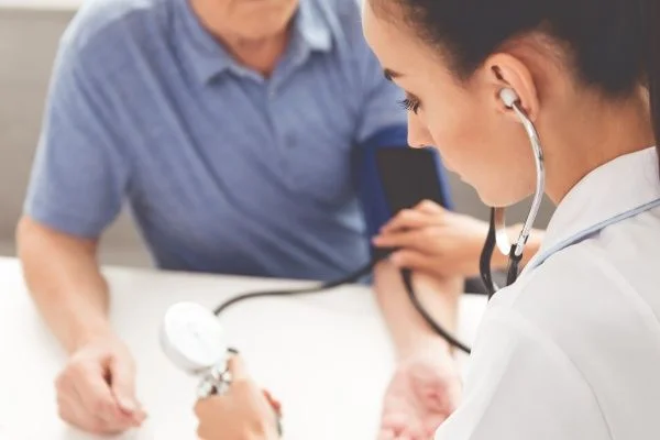 A young female nurse practitioner taking the blood pressure of an older male patient