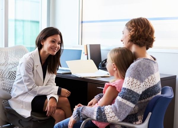 Smiling family nurse practitioner sitting across from mother and daughter patients in her office