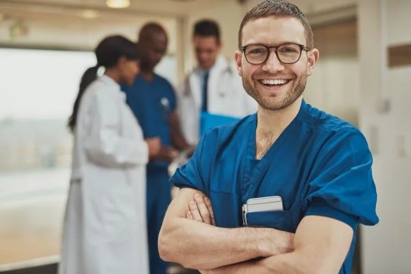 Male nurse smiling with arms crossed in a hospital setting