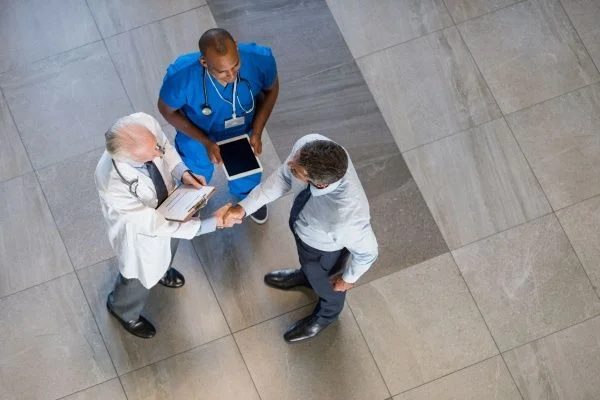 Overhead view of two male doctors shaking hands and a male nurse