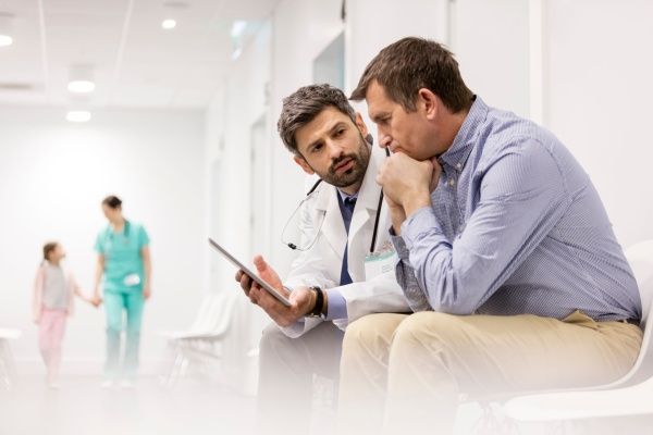 Male nurse practitioner reviewing health information with a male patient in a hospital corridor