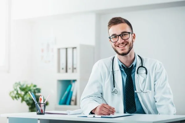 Smiling male nurse practitioner wearing a white lab coat in a white office setting