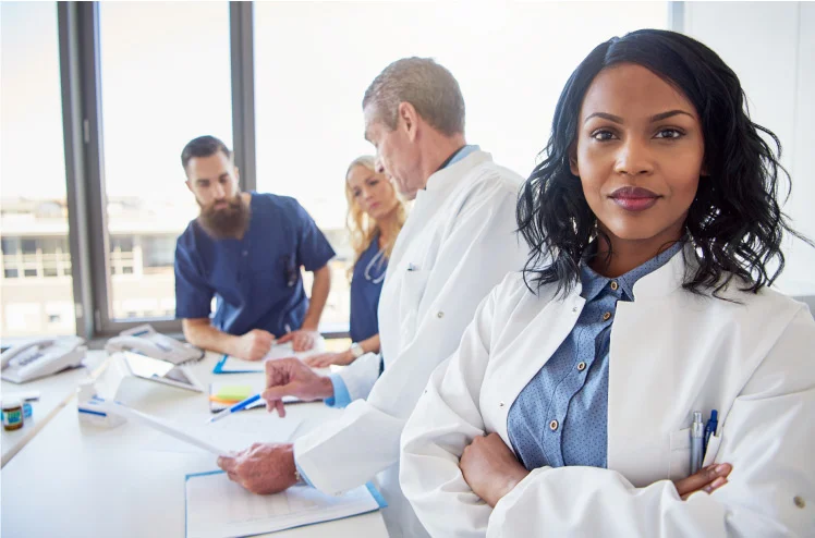 Female nurse practitioner with her arms crossed looking confident in a meeting with fellow healthcare workers