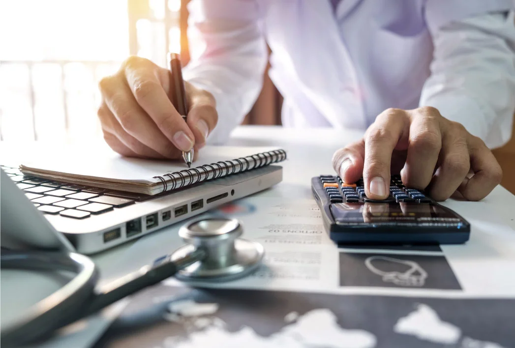 Close-up of a nurse practitioner making notes and using a calculator at her office desk