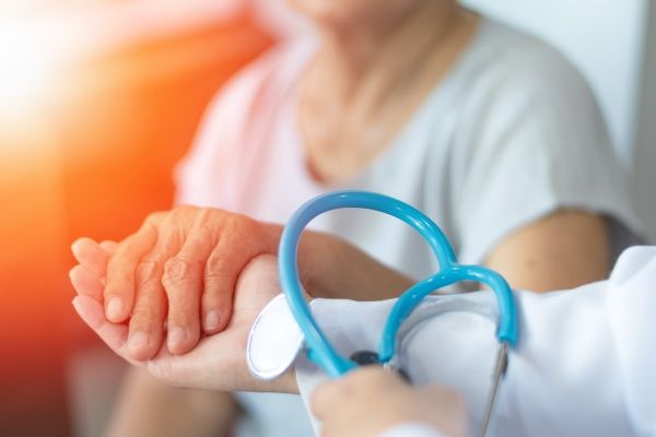 Close-up of nurse practitioner holding an elderly patient's hand and a blue stethoscope