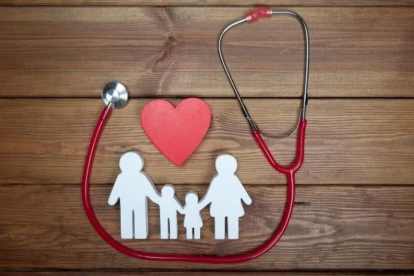 White cardboard cutout of a family with a heart above them and a stethoscope against a wooden background