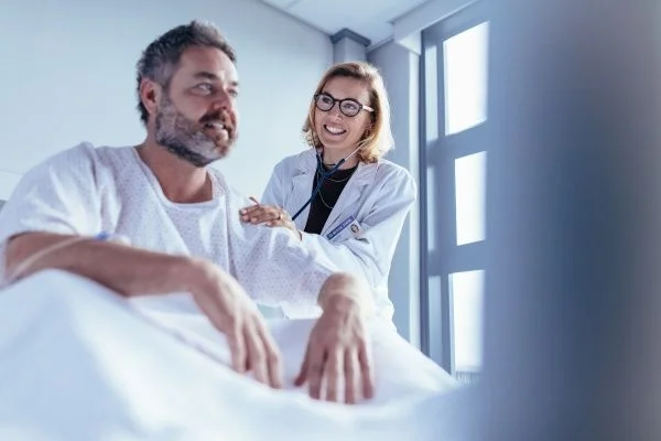 Female nurse practitioner resting her hand on the arm of a male patient in a hospital bed