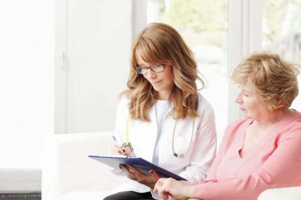 Female nurse practitioner meeting with a middle-aged female patient and making notes on a clipboard
