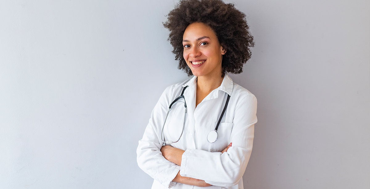 Confident nurse practitioner leans against wall with arms crossed