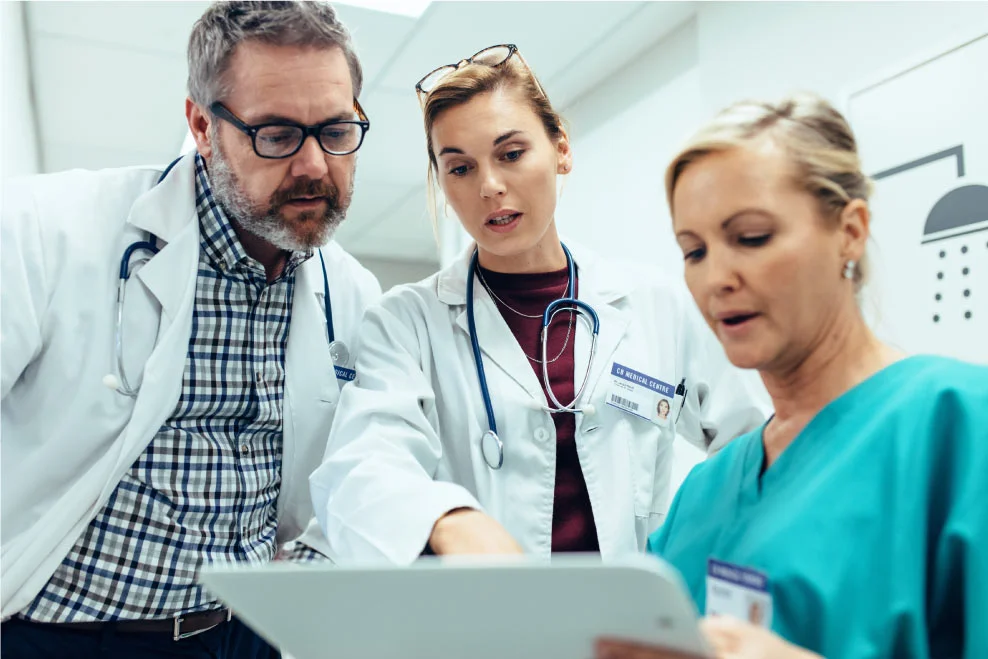 Healthcare workers discussing a patient's condition while reviewing notes on a clipboard