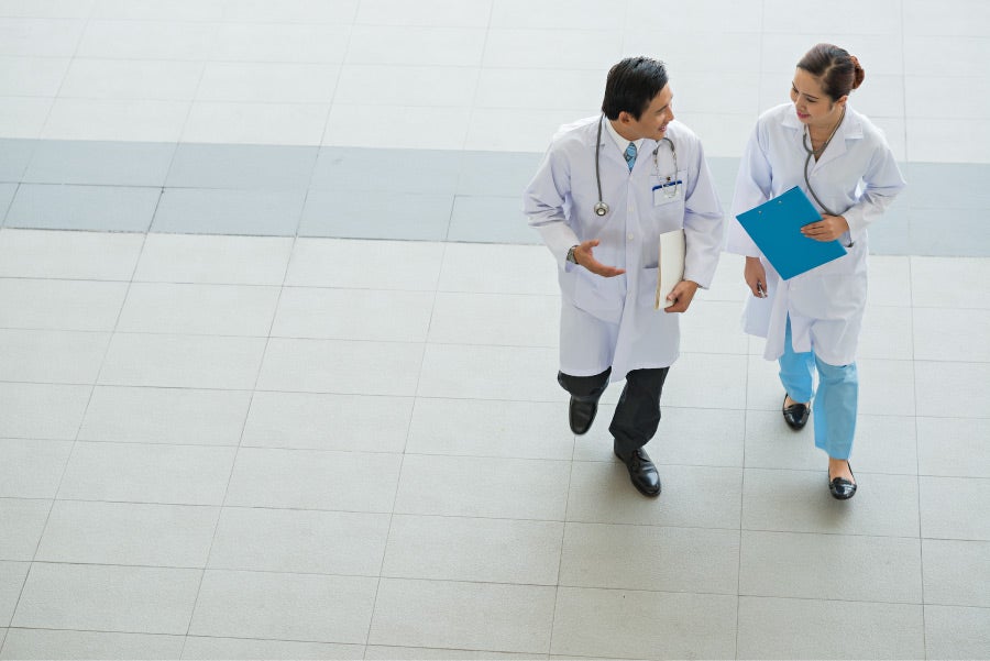 Two nurse practitioners in white lab coats walking and talking
