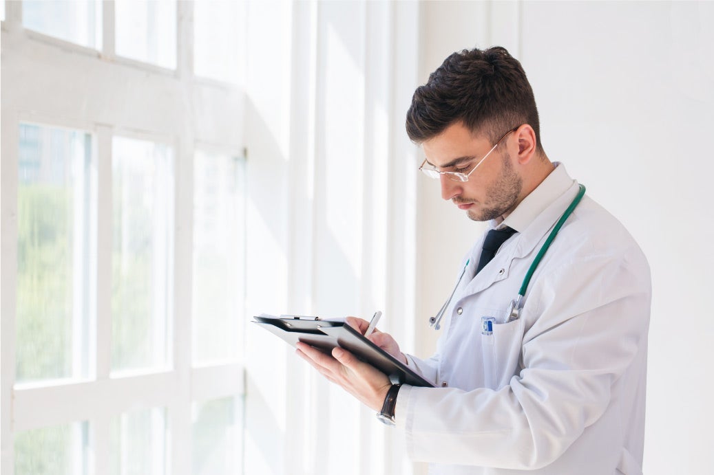 Male nurse practitioner making notes on a clipboard in brightly lit office