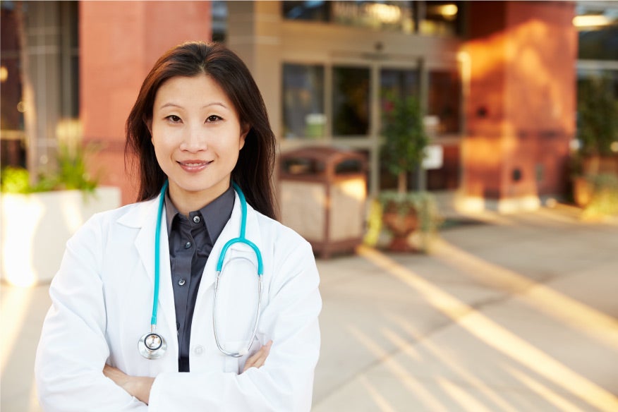 High earning female family nurse practitioner standing in front of a hospital looking confident