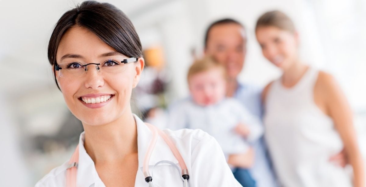 Smiling female nurse practitioner with a family standing in the background