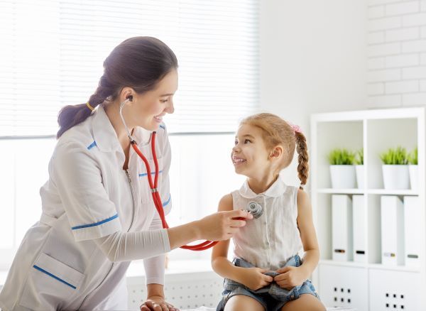 Smiling female nurse practitioner using a stethoscope on a young girl