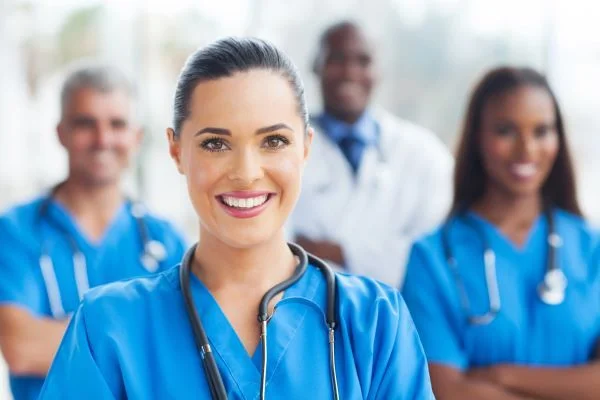 A group of smiling nurses standing in front of a doctor with their arms crossed