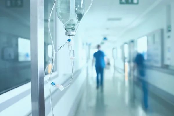 An IV drip in a hospital corridor with a nurse walking in the background