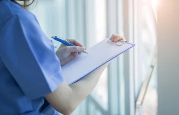 Close-up of a nurse writing on a clipboard