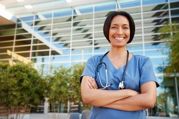 Smiling nurse standing outside of a hospital with her arms crossed