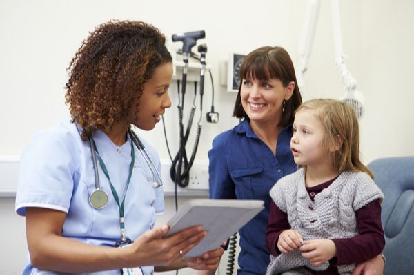 Female nurse practitioner interacting with a young girl patient and her mother