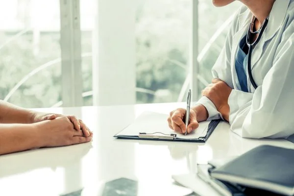 Close-up of a nurse practitioner writing notes in her office while talking to a patient