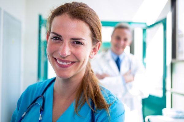 Smiling nurse in blue scrubs with doctor standing behind her